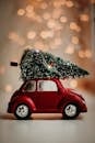 A red toy car carries a Christmas tree, set against a warm bokeh background, celebrating the festive season.